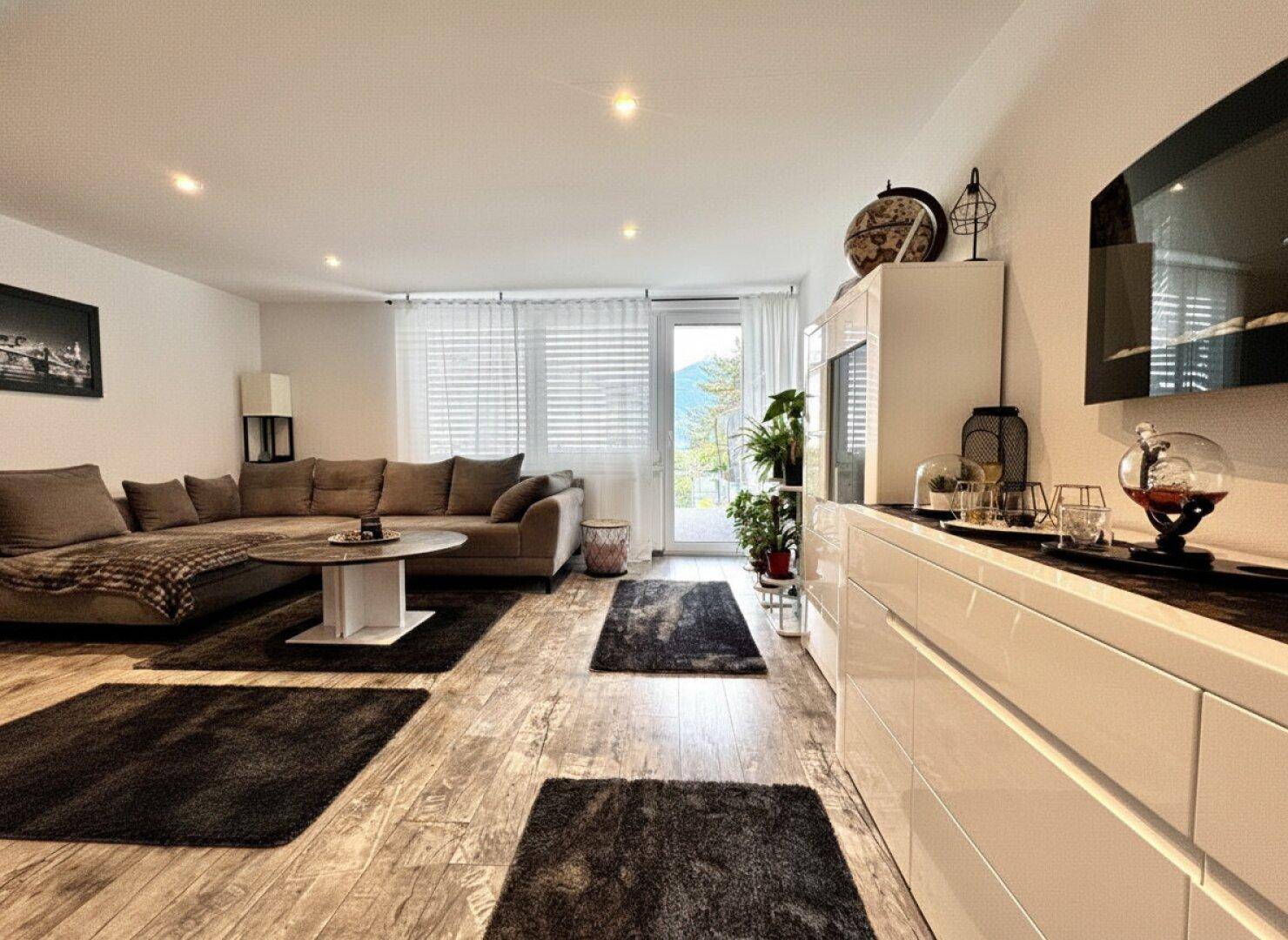 Geräumiges Wohnzimmer mit großem Ecksofa, Holzboden und Zugang zu einem Balkon.