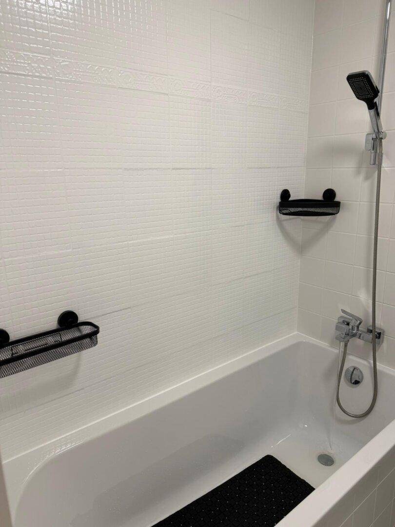 Nahaufnahme einer Badewanne mit Duscharmatur und weißen Wandfliesen in einem modernen Badezimmer.
