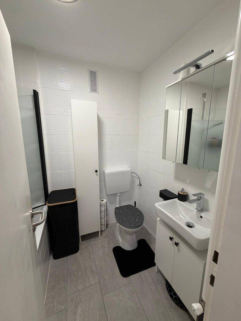 Modernes Badezimmer mit weißen Fliesen, Toilette, Waschbecken und einer Badewanne.