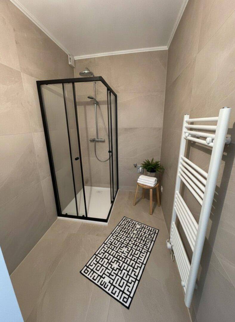 Modernes Badezimmer mit begehbarer Dusche, beigen Fliesen und Handtuchheizkörper.