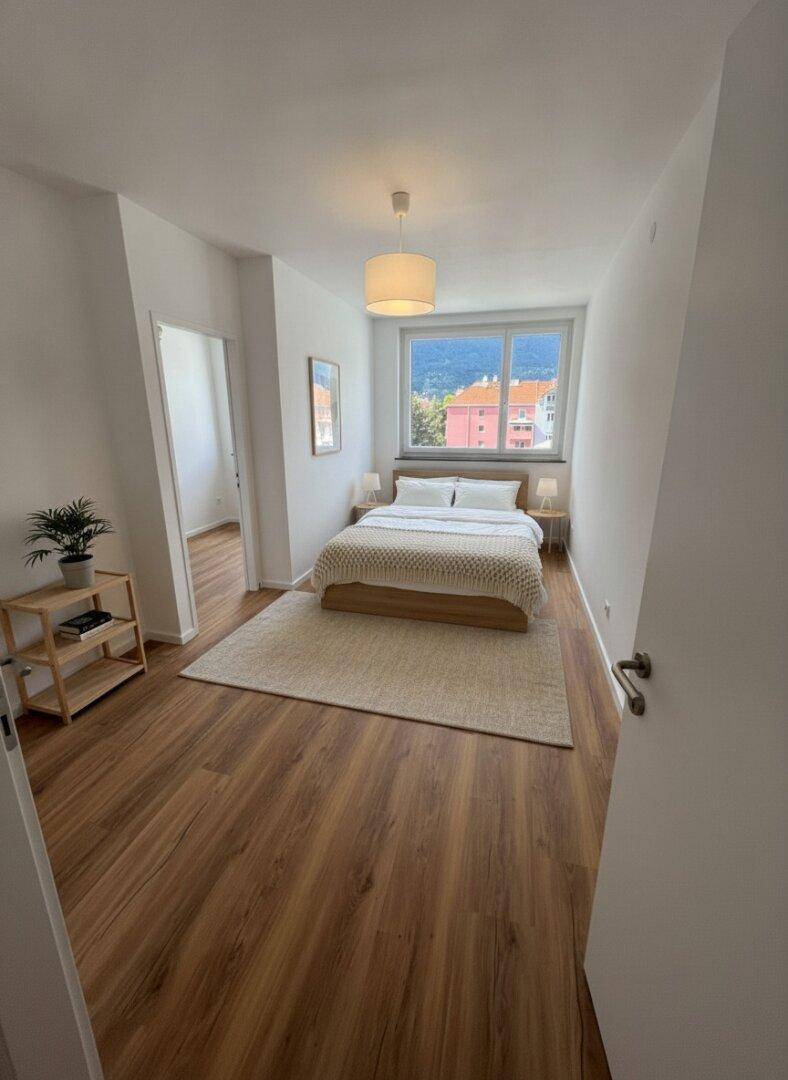 Gemütliches Schlafzimmer mit Holzbett, Laminatboden und Bergblick durch das Fenster.