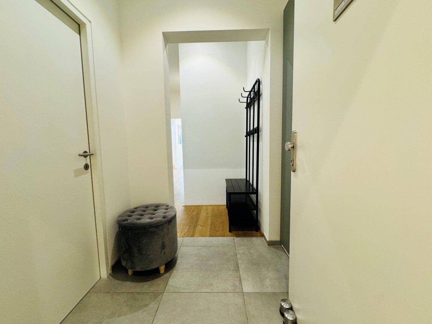 Moderner Eingangsbereich mit grauen Fliesen, Garderobe und schlichten weißen Türen.