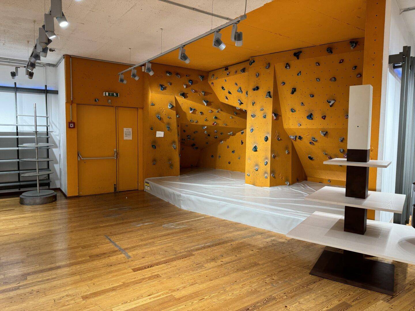 Innenbereich mit einer orangefarbenen Kletterwand und Holzboden.