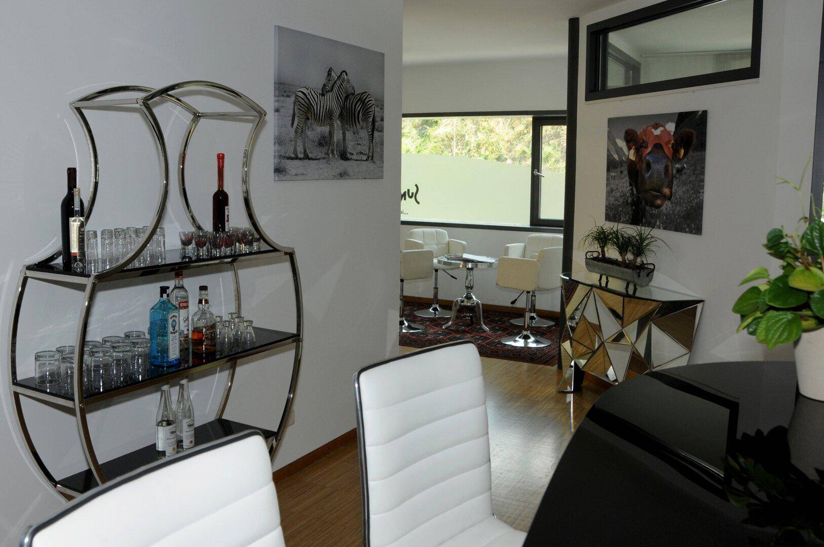 Moderner Loungebereich mit einem eleganten Getränkeregal, Kunstwerken und einem Blick in den Wartebereich.