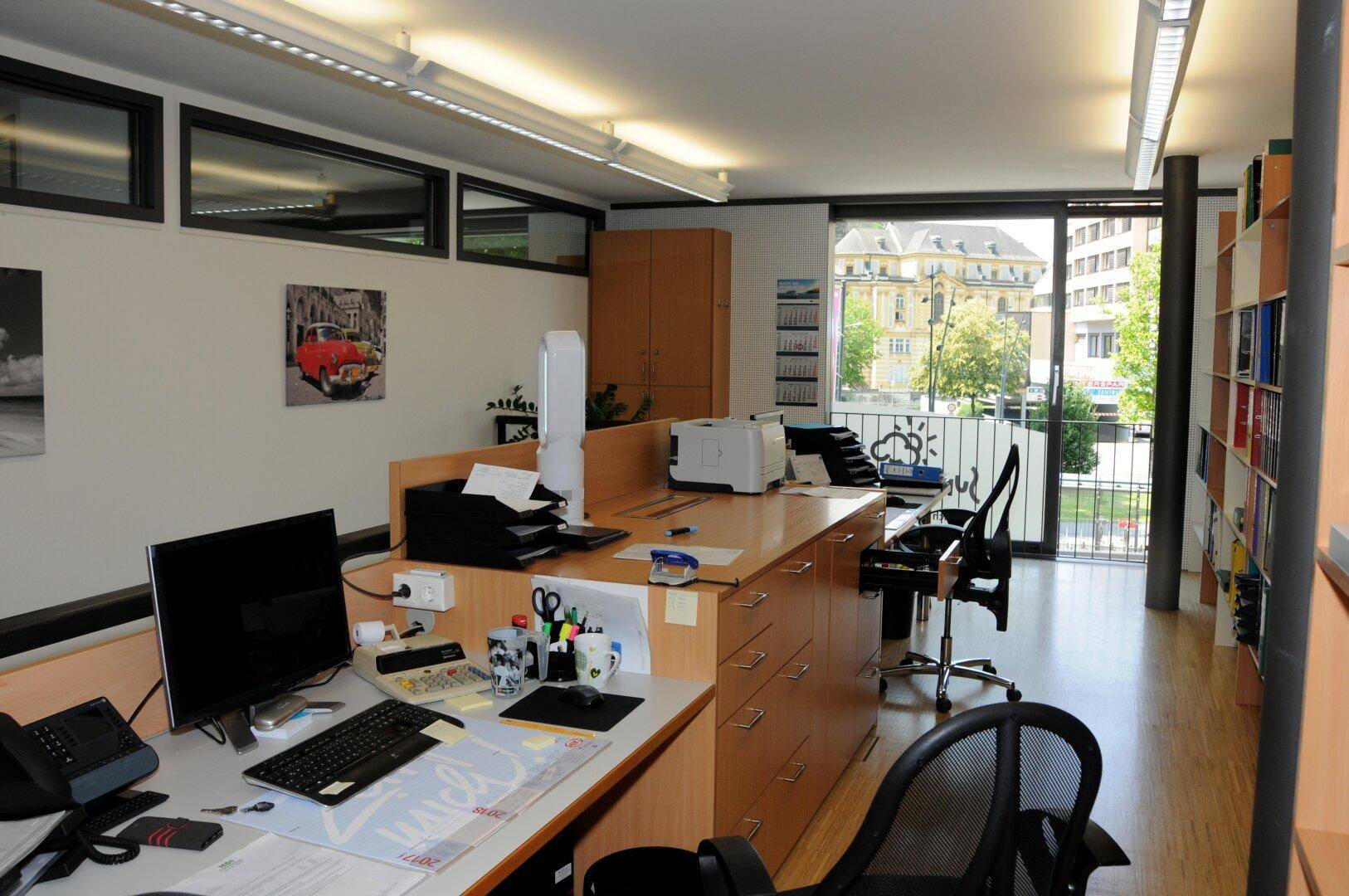 Geräumiges Büro mit mehreren Arbeitsplätzen, Holzmöbeln und einem Balkon mit Blick auf die Stadt.