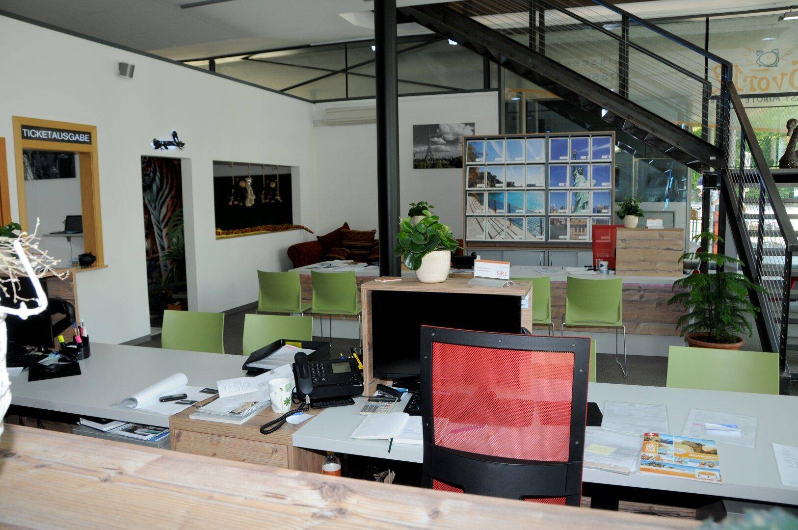 Offener Empfangsbereich mit einer modernen Metalltreppe, Schreibtischen und einem gemütlichen Sitzbereich im Hintergrund.