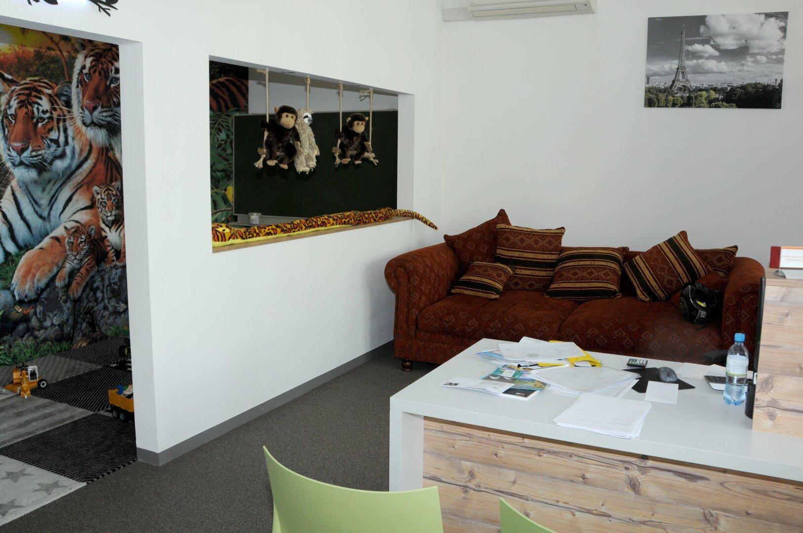 Gemütlicher Loungebereich mit einem braunen Sofa, dekorativen Kissen und einer Wand mit Tiermotiven.