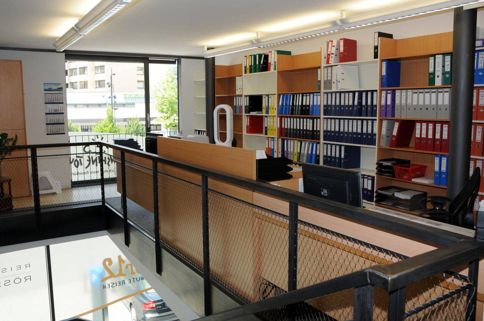 Obergeschoss-Büro mit vielen Aktenregalen, Arbeitsplätzen und einem Geländer mit Blick nach unten.