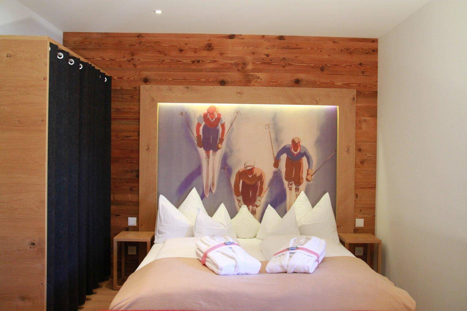 Gemütliches Schlafzimmer mit großem Bett, Holzkopfteil und Skifahrer-Motiv.