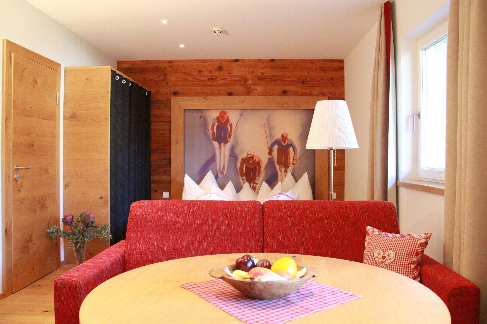 Schlafzimmer im alpinen Stil mit rotem Sofa, rundem Tisch und Skifahrer-Wandbild.