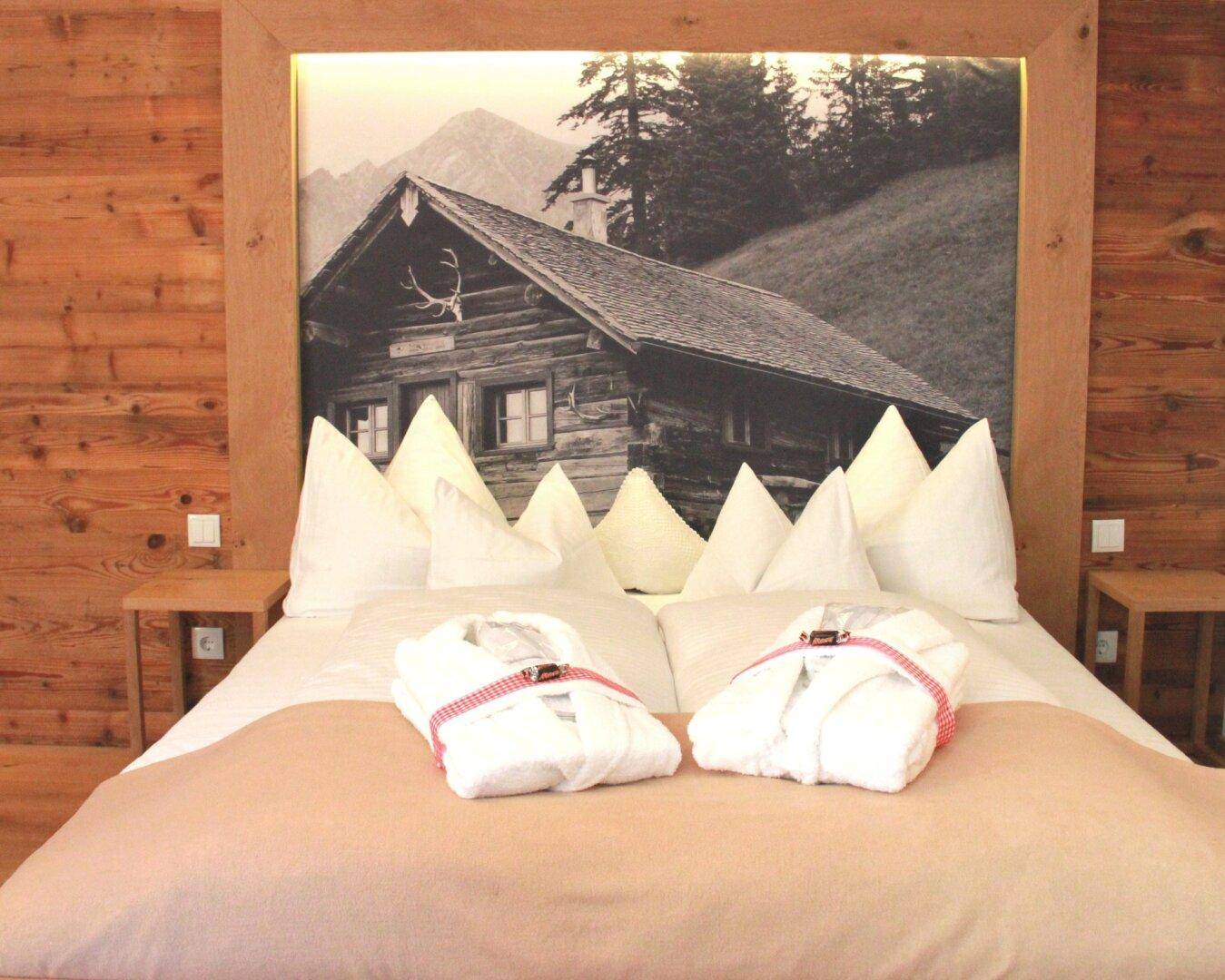 Schlafzimmer mit großem Bett, Holzkopfteil und Schwarz-Weiß-Bild einer Berghütte.