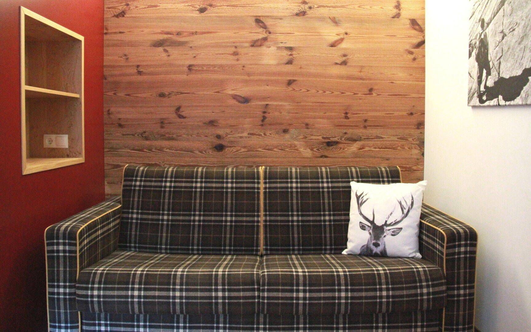 Gemütlicher Wohnbereich mit kariertem Sofa und rustikaler Holzwandverkleidung.