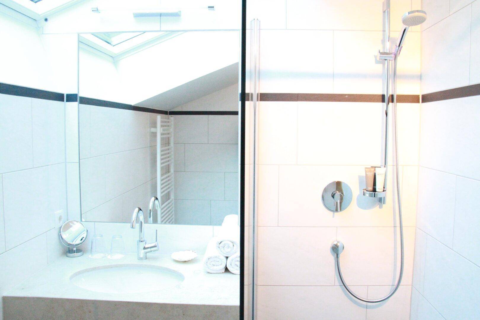 Helles Badezimmer mit Einzelwaschbecken, großem Spiegel und moderner Dusche.