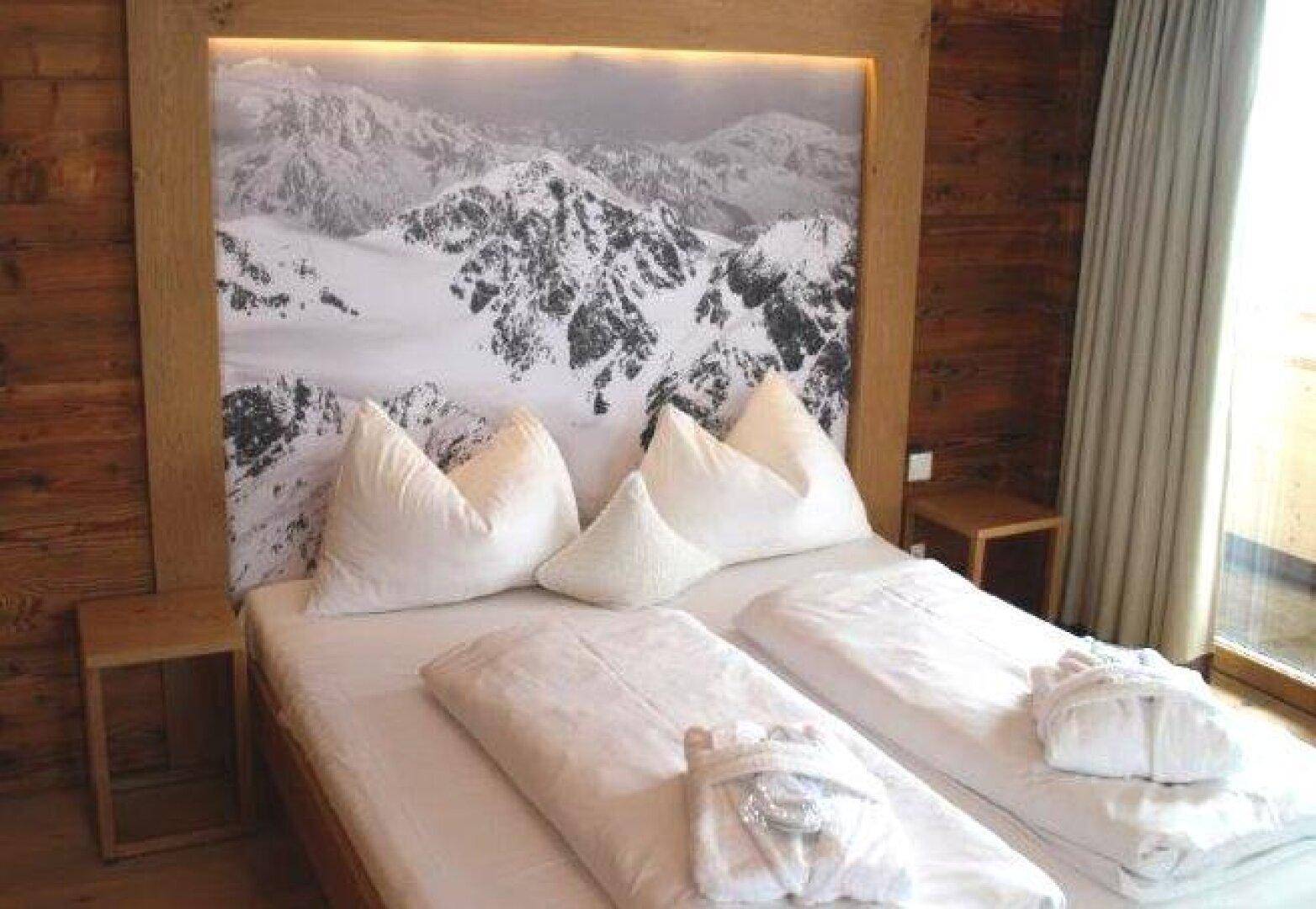 Schlafzimmer mit zwei Einzelbetten, Holzkopfteil und verschneitem Bergpanorama.