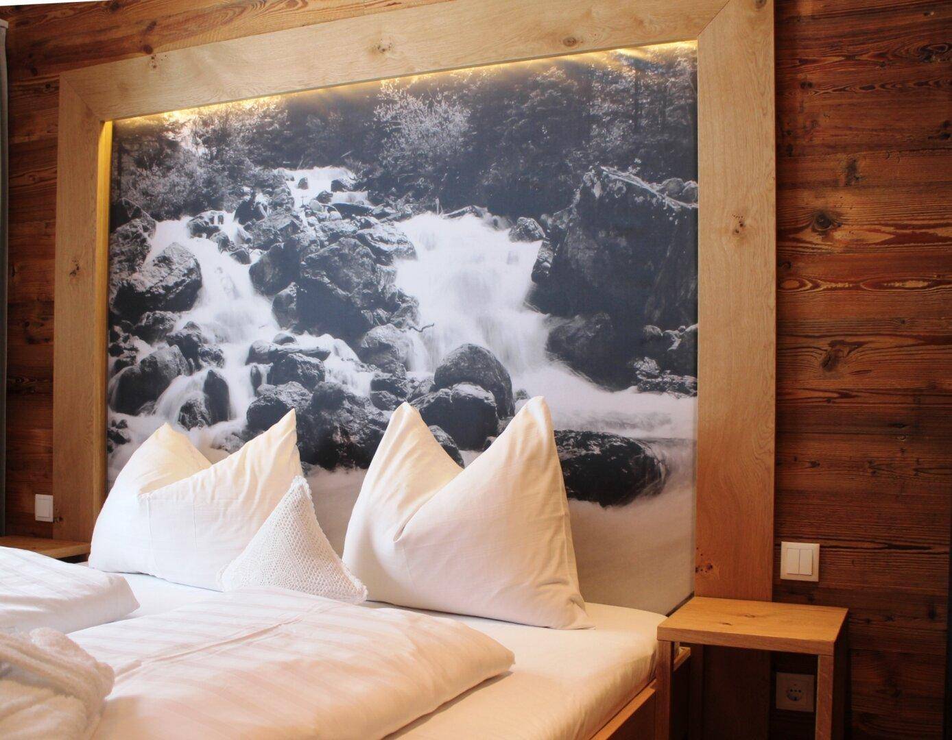 Schlafzimmer mit großem Bett, Holzkopfteil und Schwarz-Weiß-Bild eines Wasserfalls.