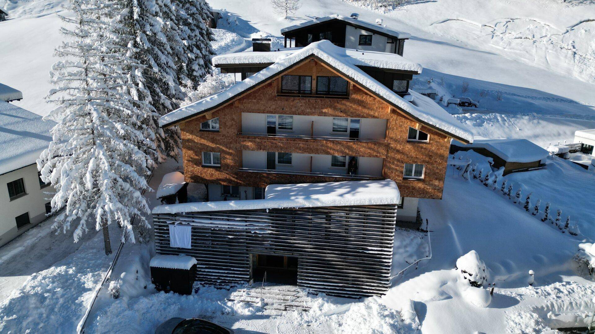Winterliche Luftaufnahme des Holzchalets, eingebettet in eine verschneite Berglandschaft.