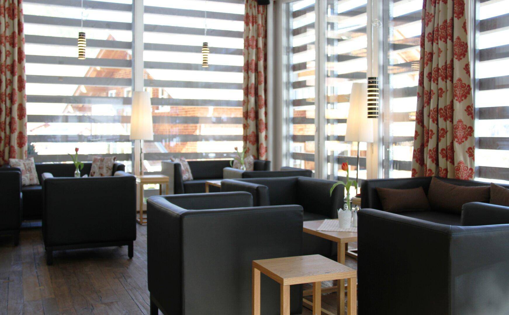 Geräumiger Loungebereich mit bequemen schwarzen Sofas und großen Fenstern.