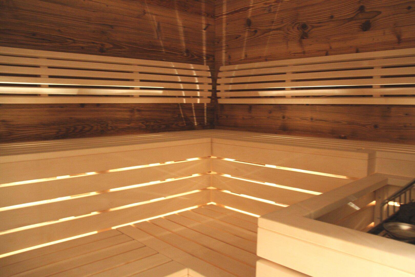 Innenansicht einer traditionellen Holzsauna mit mehrstufigen Bänken und einem Saunaofen in der Ecke.