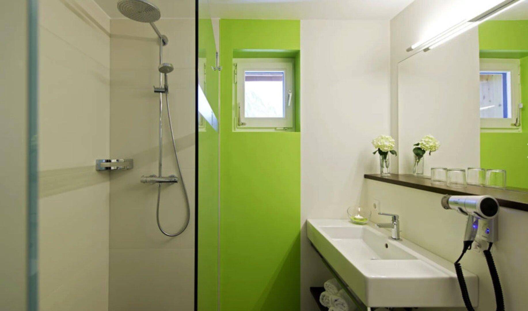 Helles Badezimmer mit moderner Dusche, Waschbecken und einem Fenster, akzentuiert durch grüne Wandfarbe.