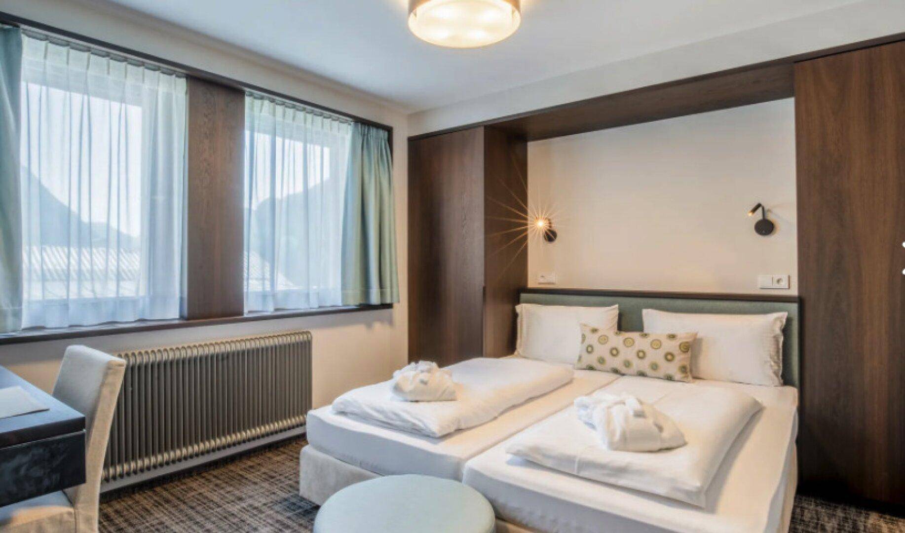 Komfortables Schlafzimmer mit zwei Betten, einem Schreibtisch und einem weiten Blick auf die Berge.