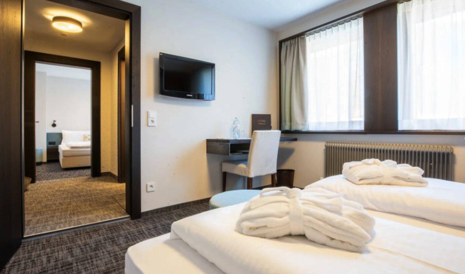 Gemütliches Schlafzimmer mit zwei Betten, einem Schreibtisch und Blick in ein angrenzendes Zimmer.