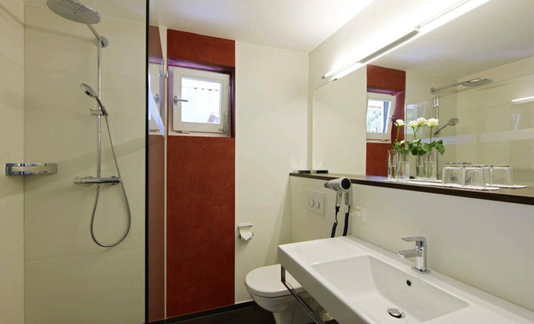Funktionales Badezimmer mit Dusche, Waschbecken und Fenster für natürliche Belüftung.