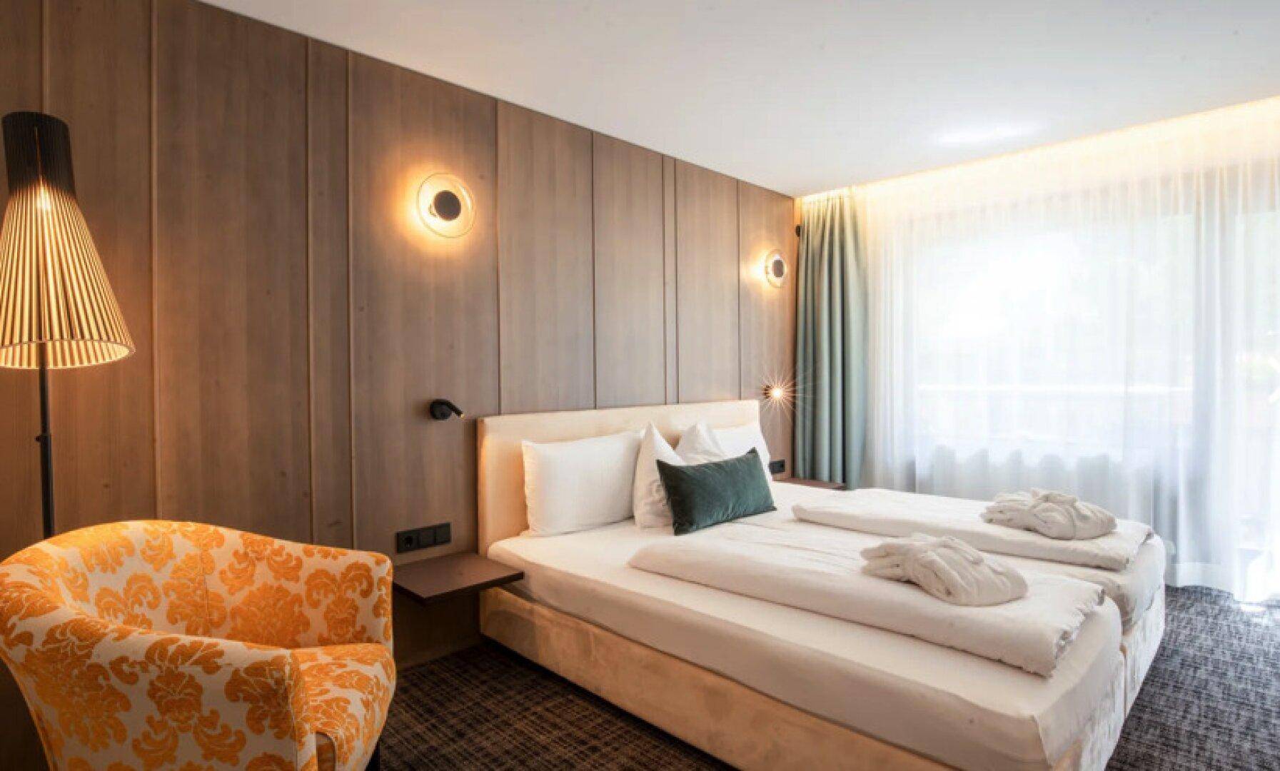 Modernes Schlafzimmer mit Holzwandverkleidung, zwei Einzelbetten und einem gemusterten Sessel.