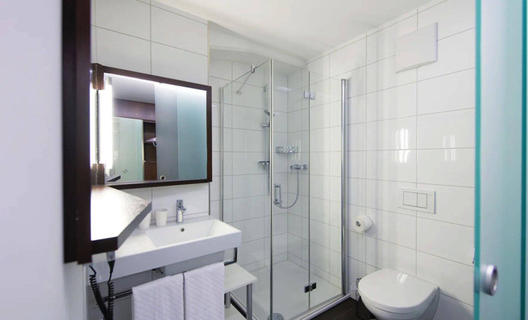 Kleines, helles Badezimmer mit weiß gefliesten Wänden, einer Glasdusche und einem modernen Waschbecken.
