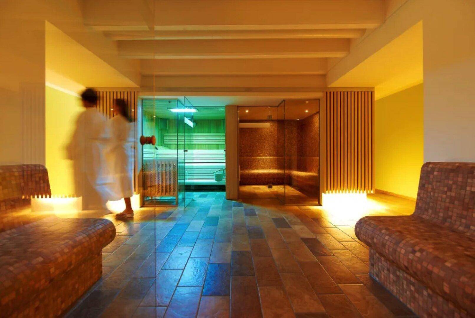 Entspannender Wellnessbereich mit Sauna und Dampfbad, beleuchtet in warmen Farbtönen.