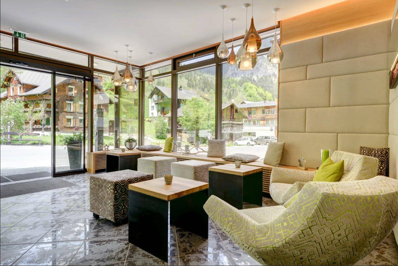 Moderne Hotellobby mit großen Fenstern, bequemen Sitzgelegenheiten und Blick auf die Berge.