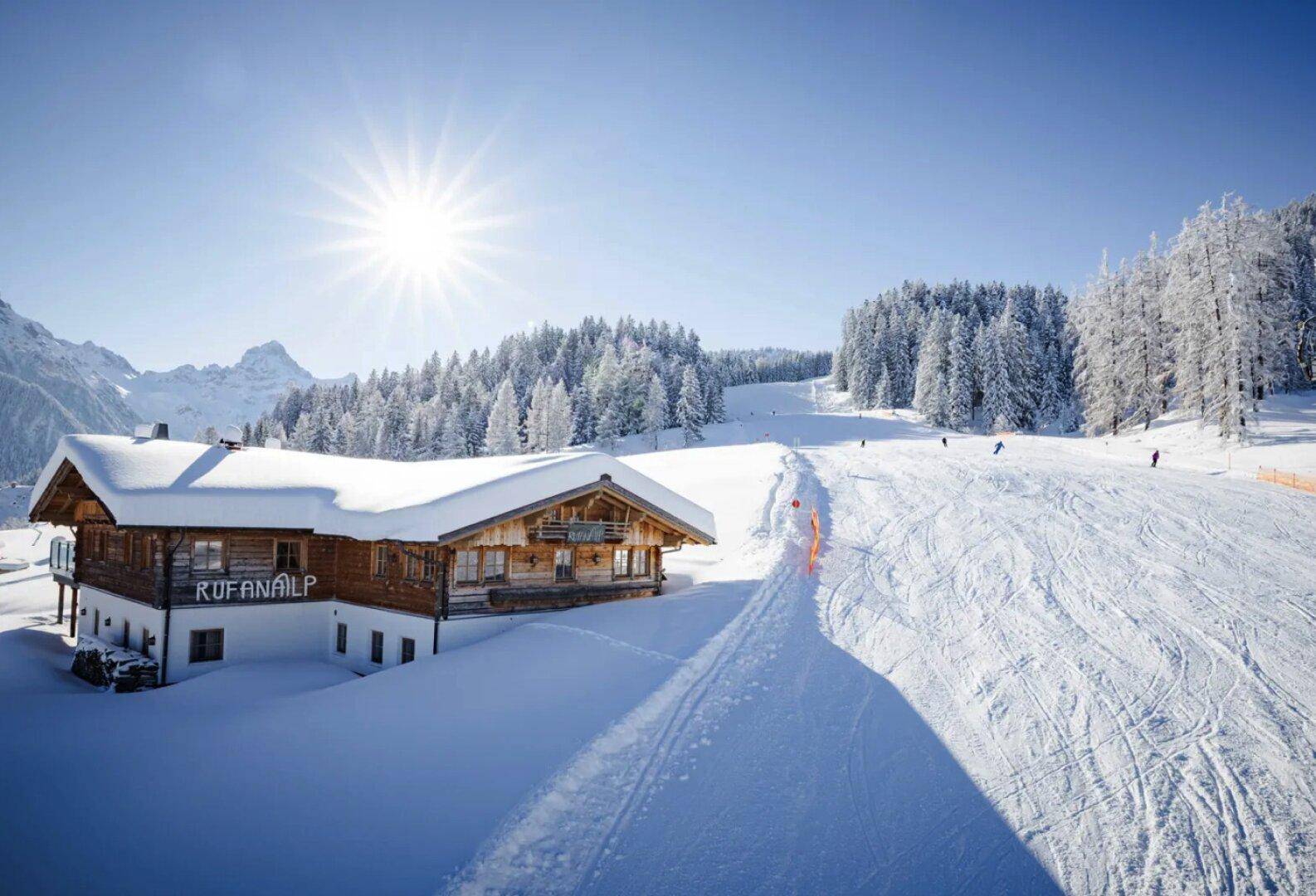 Eine verschneite Berghütte in einem Skigebiet unter strahlend blauem Himmel und Sonnenschein.