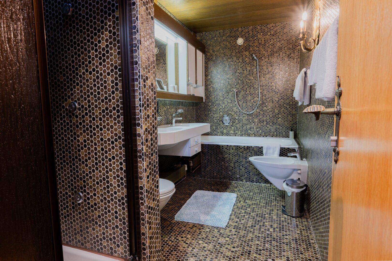 Badezimmer mit auffälligen Mosaikfliesen an Wänden und Boden, ausgestattet mit Dusche und Badewanne.