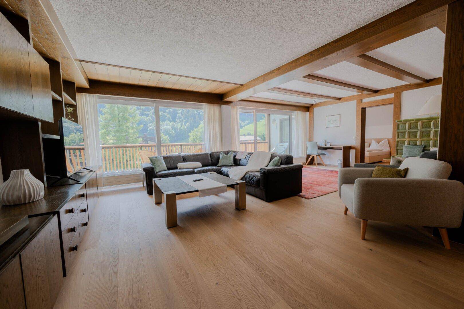 Geräumiges Wohnzimmer mit Holzbalken, großen Fenstern und Blick auf die grüne Landschaft.