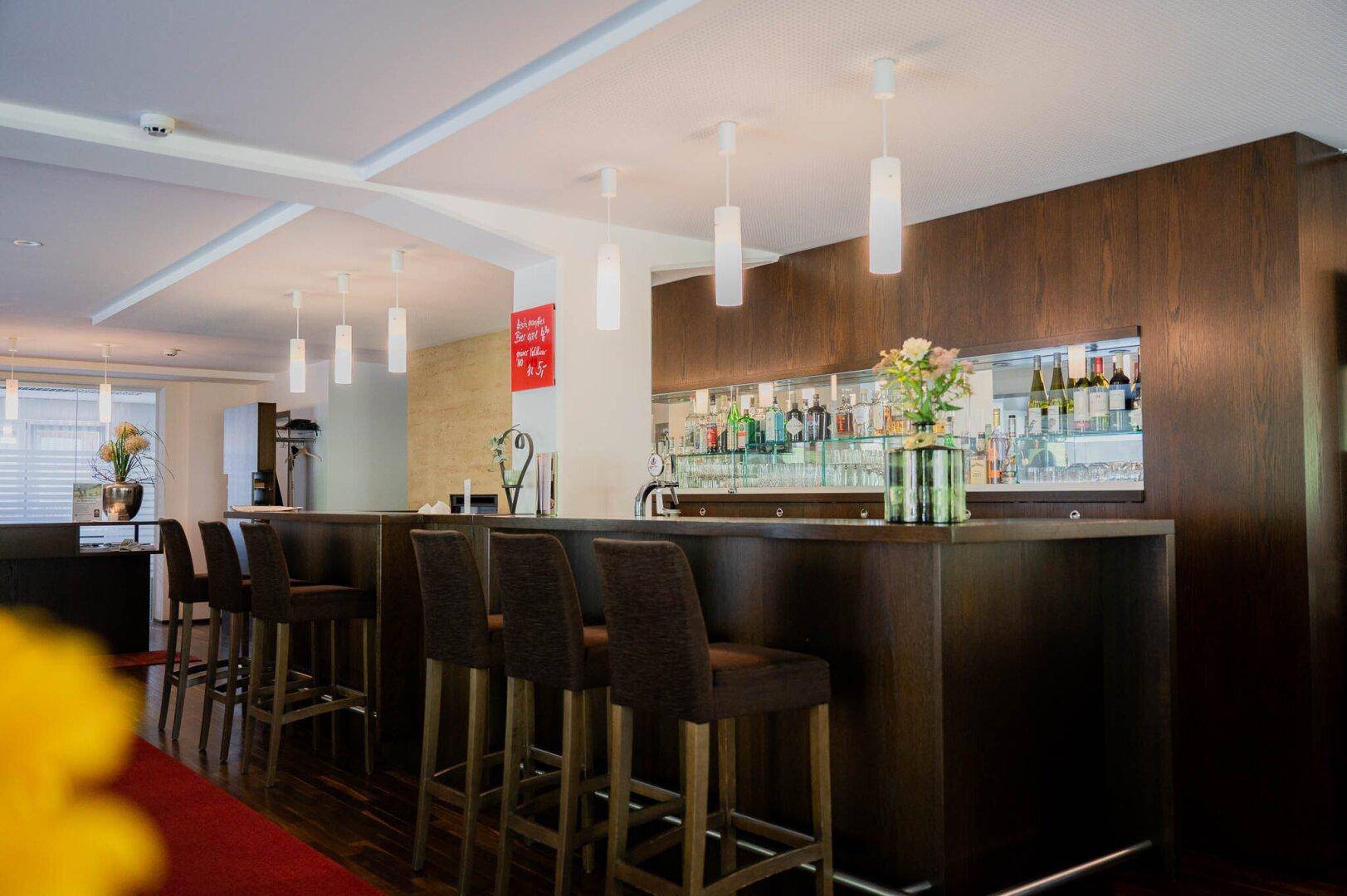Elegante Hotelbar mit dunkler Holzverkleidung, Barhockern und einer gut sortierten Getränkeauswahl.