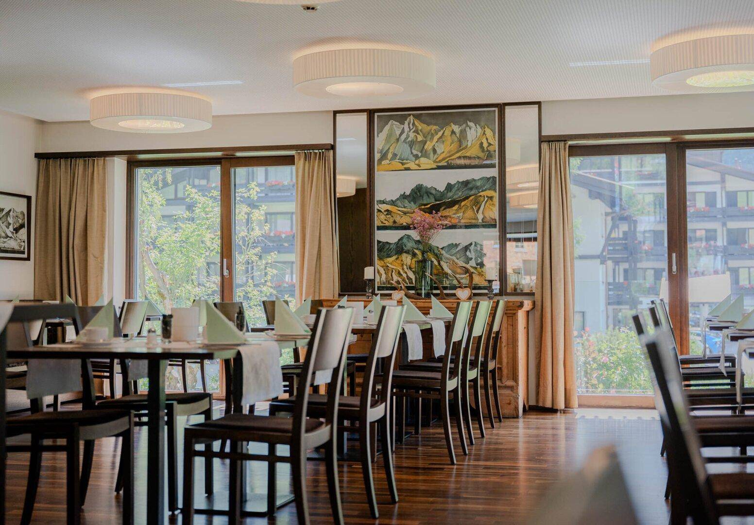 Geräumiger Speisesaal mit Holzboden, großen Fenstern und elegant gedeckten Tischen.