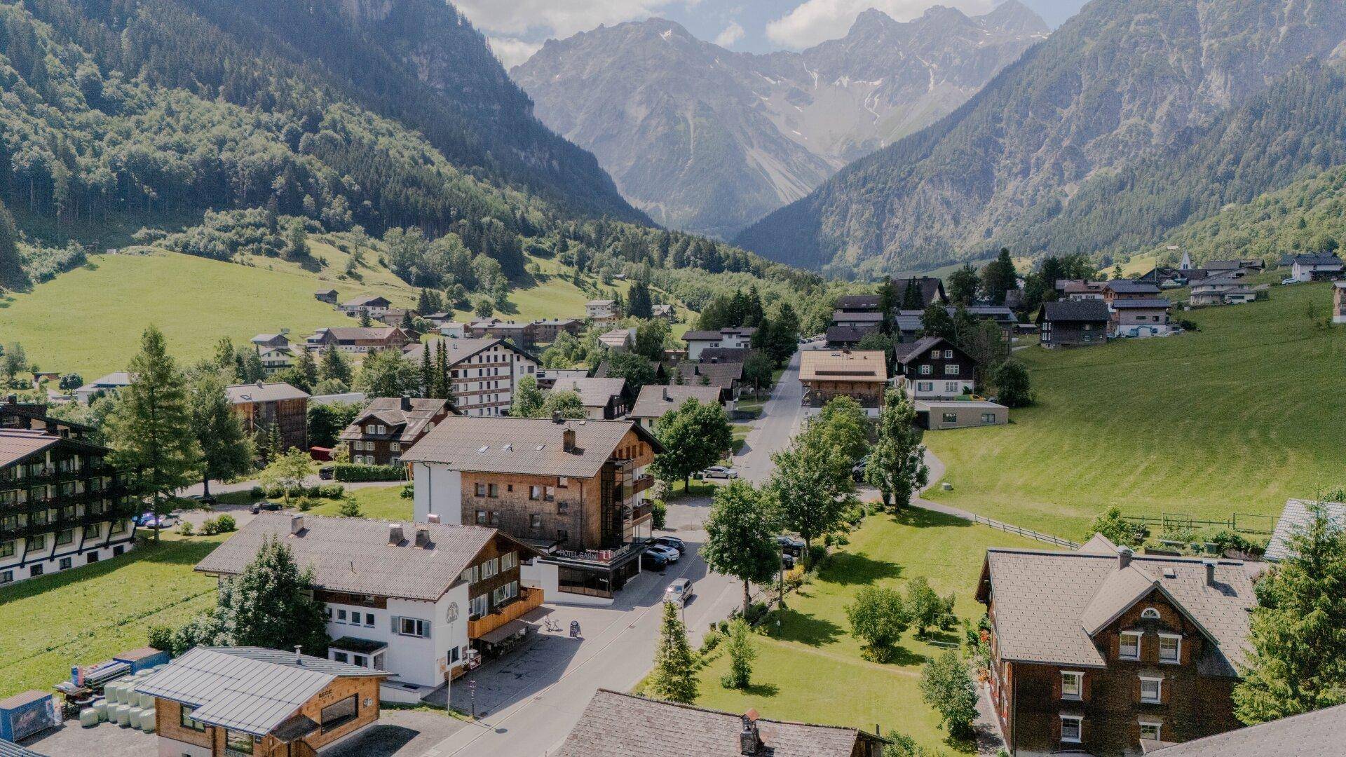 Weitläufige Ansicht eines Bergdorfes mit traditionellen Häusern und üppiger Vegetation im Tal.