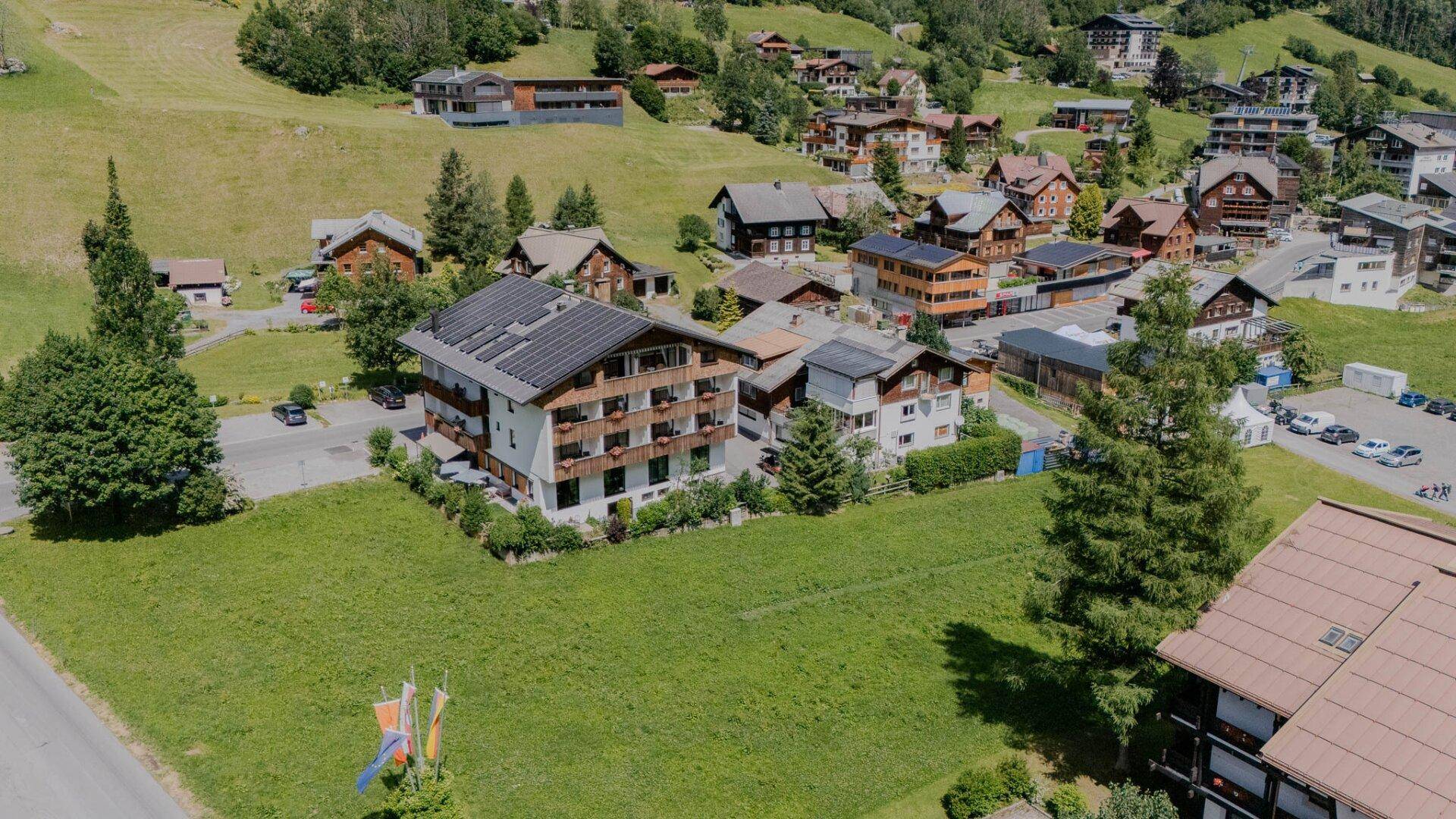 Luftaufnahme eines Gebäudekomplexes mit Solaranlagen auf dem Dach, umgeben von grünen Wiesen.