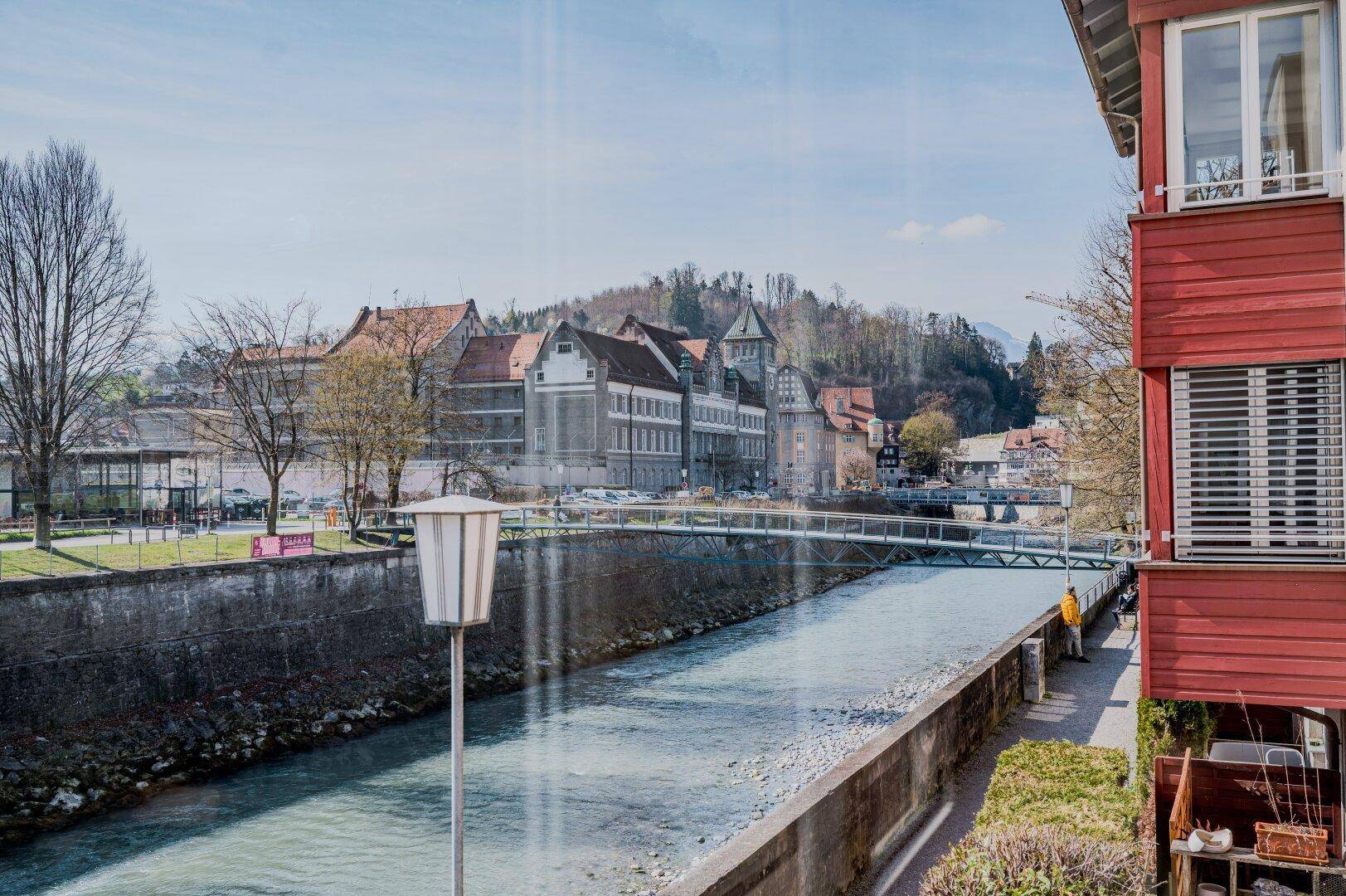 Weitblick über einen Fluss, eine Brücke und eine Stadt mit Bergen im Hintergrund.