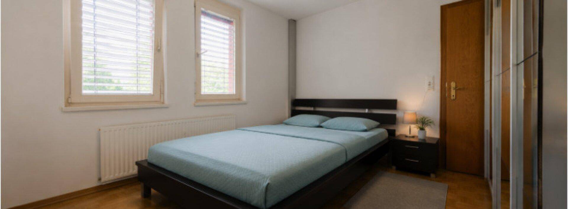 Gemütliches Schlafzimmer mit Doppelbett, zwei Fenstern und einem Kleiderschrank.