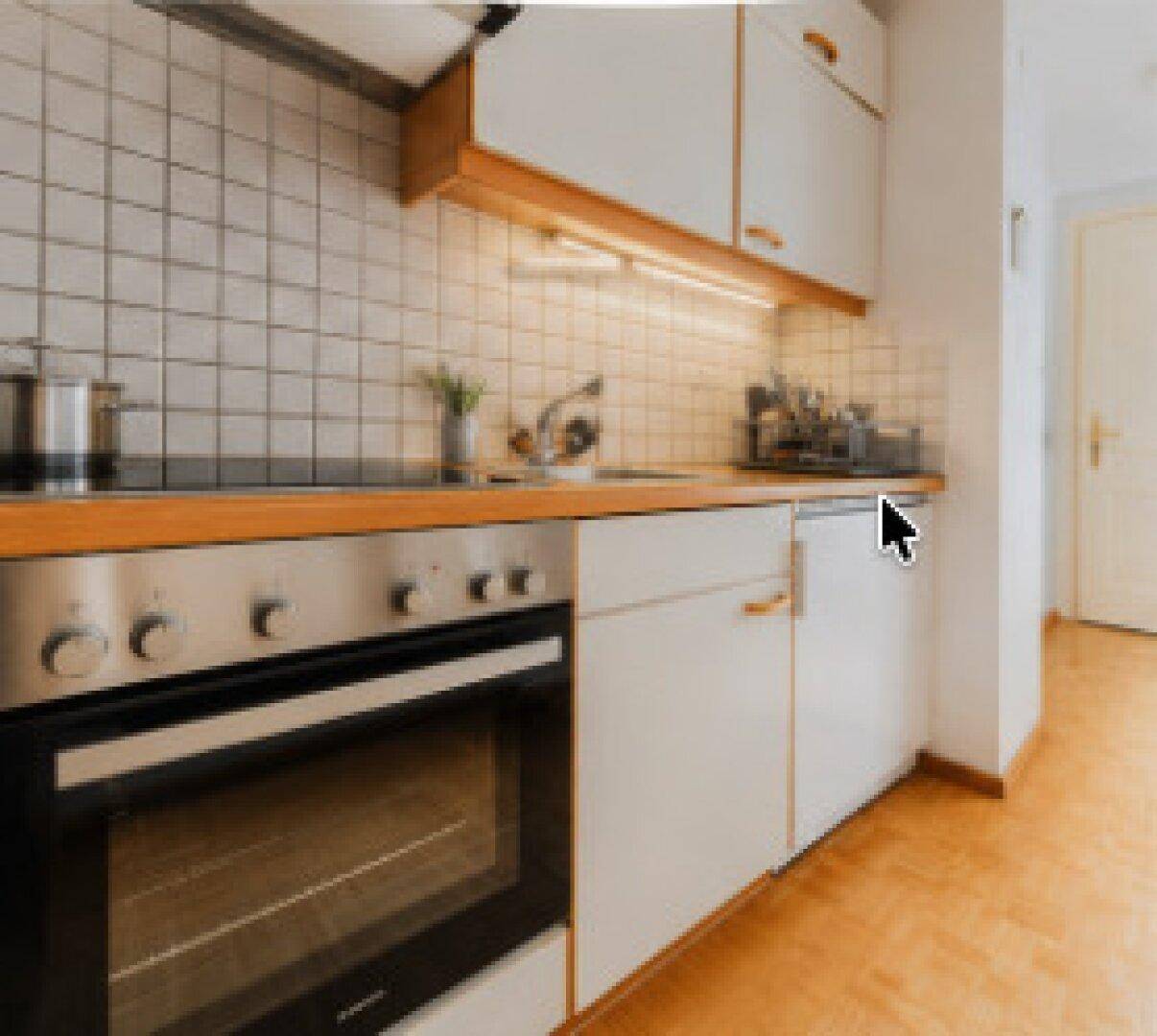 Funktionale Küche mit weißen Schränken, Holzarbeitsplatte und integriertem Backofen.