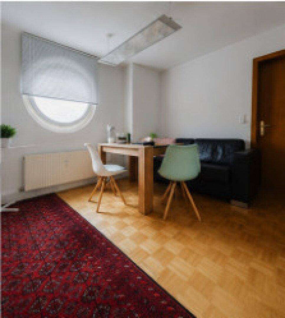 Heller Wohnbereich mit Esstisch, Sofa und einem markanten runden Fenster.