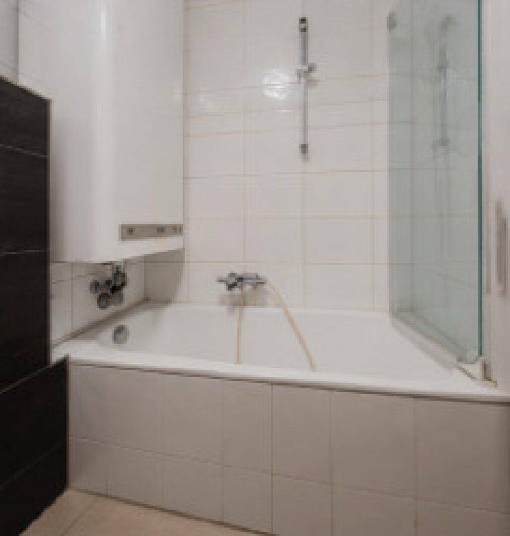 Helles Badezimmer mit Badewanne, Duschwand und weißen Fliesen.