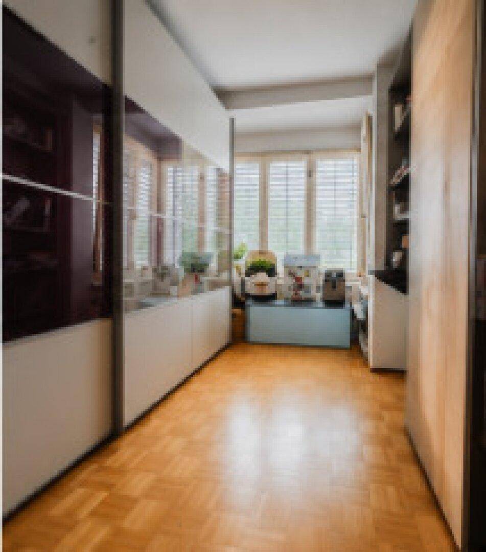 Heller Flur mit Einbauschränken und Holzparkettboden, der zu Fenstern führt.