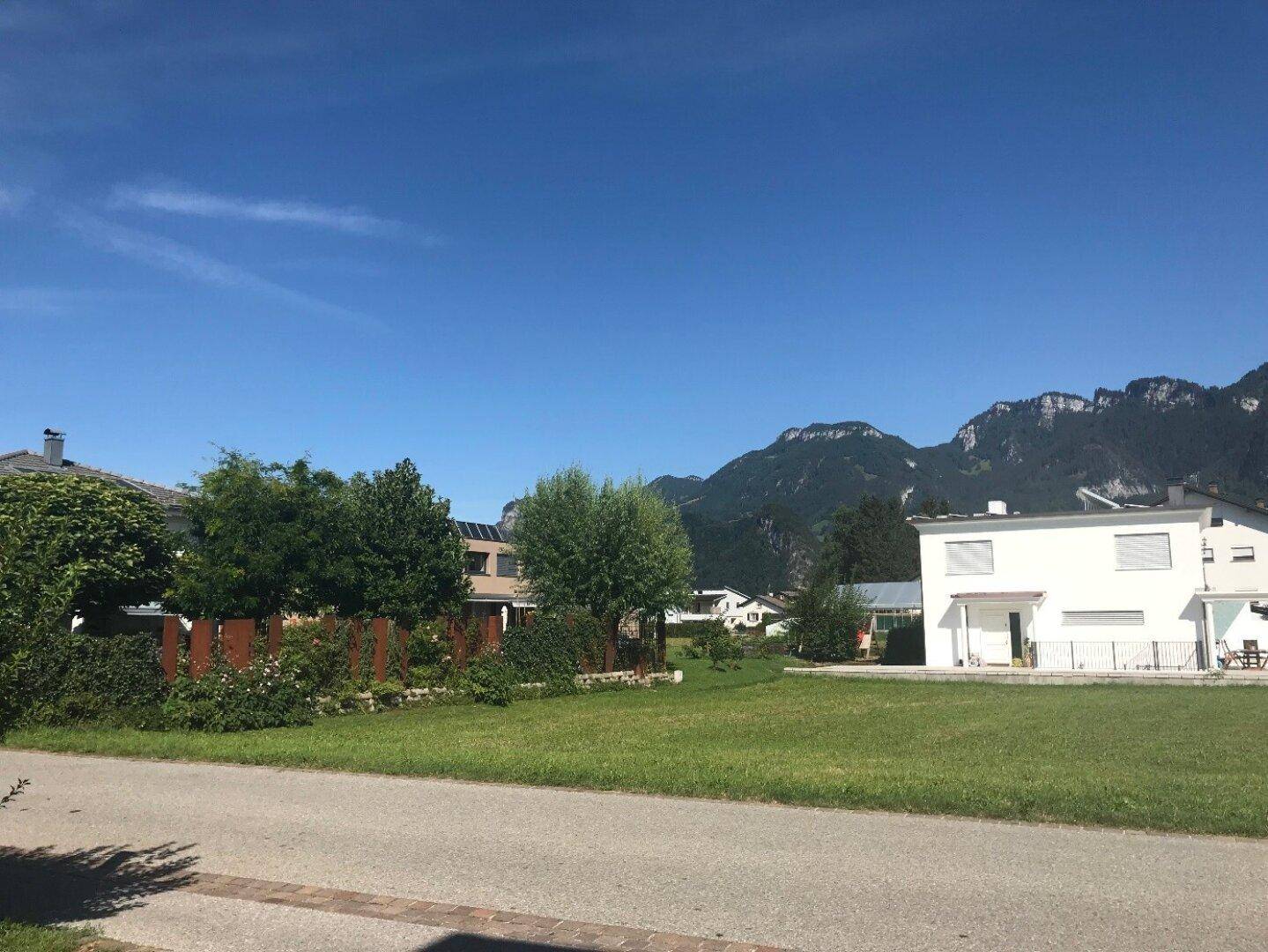 Sonnige Wohngegend mit modernen Häusern, grünen Flächen und beeindruckendem Bergblick.