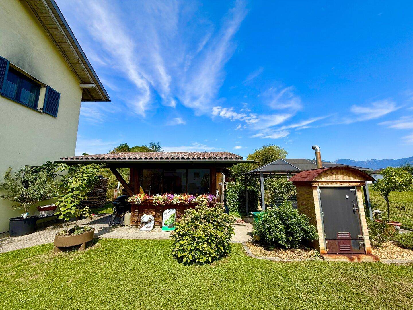 Gemütlicher Gartenbereich mit überdachtem Sitzplatz, Grillbereich und einer kleinen Sauna.