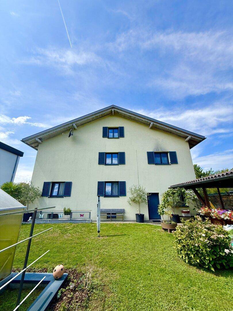 Rückseite des Hauses mit großem Rasen, einer Bank und Blick auf die umliegende Natur.