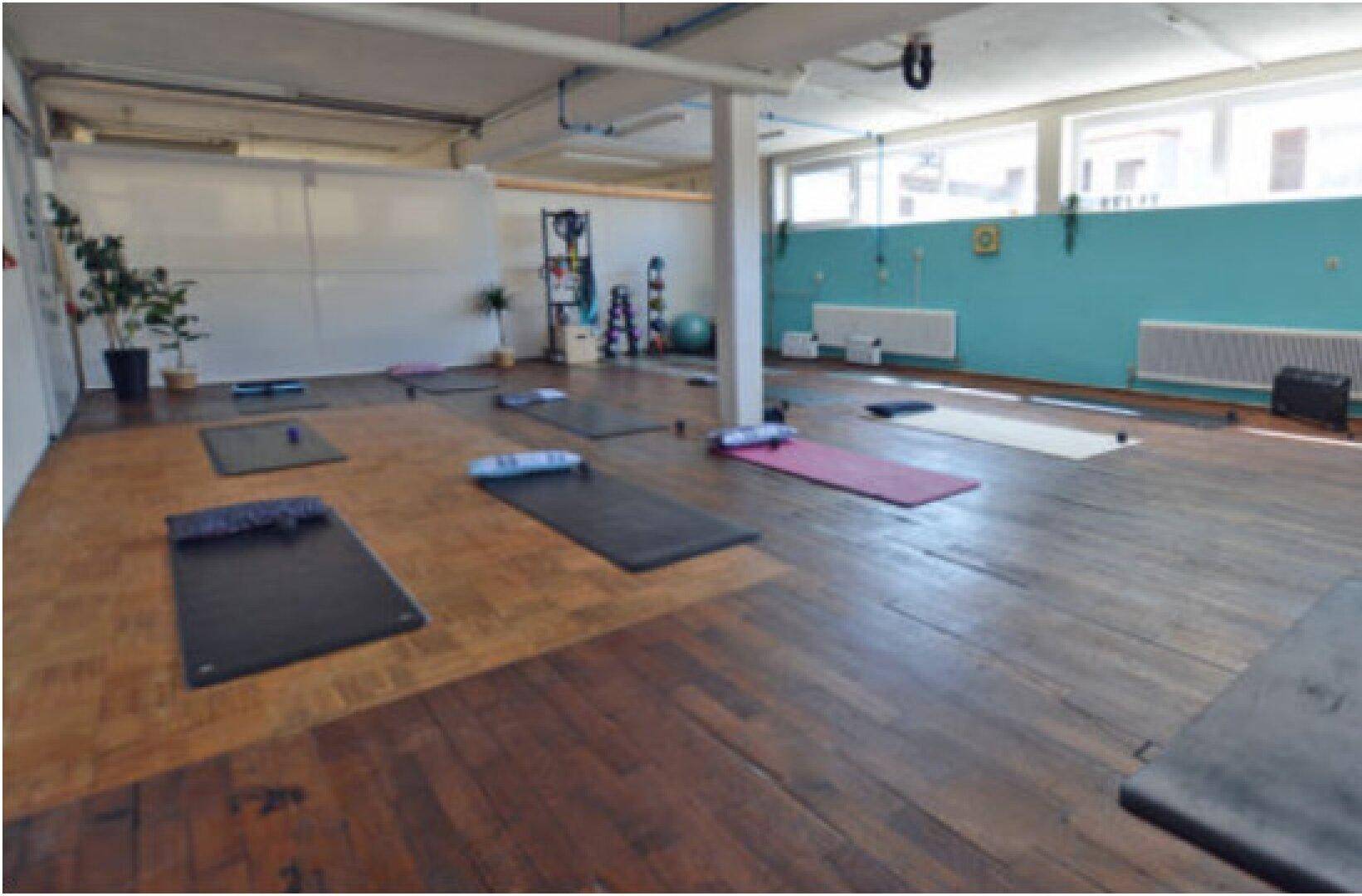 Großer Raum, eingerichtet als Yoga- oder Fitnessstudio, mit Holzdielenboden und tealfarbener Wand.