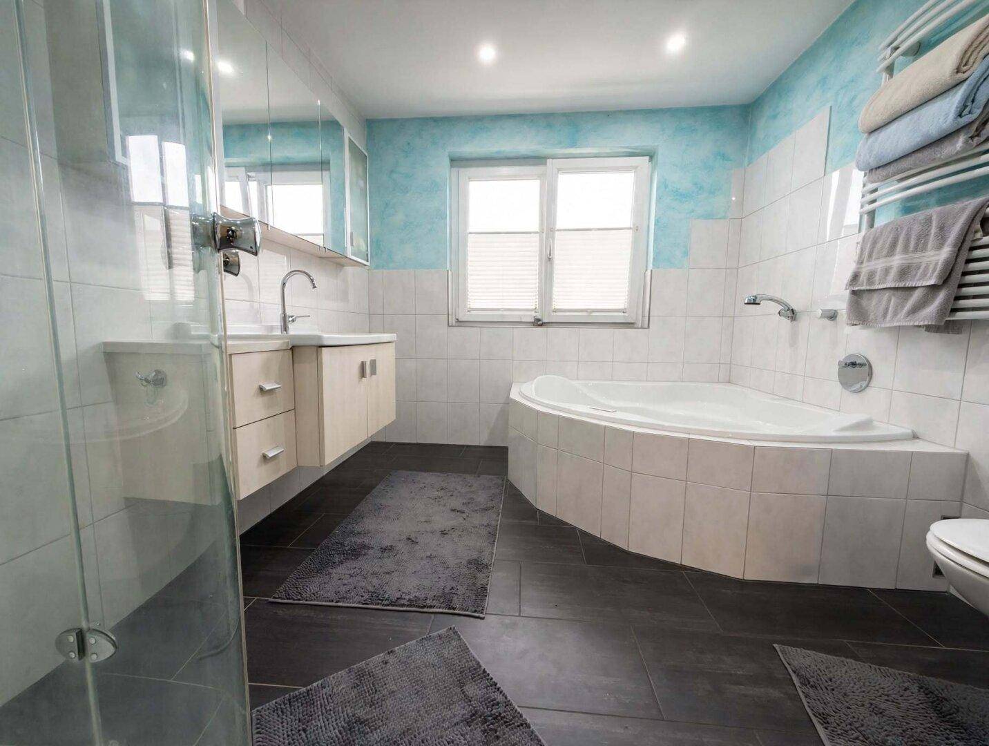 Geräumiges Badezimmer mit Eckbadewanne, Duschkabine, Doppelwaschbecken und blauen Akzenten.