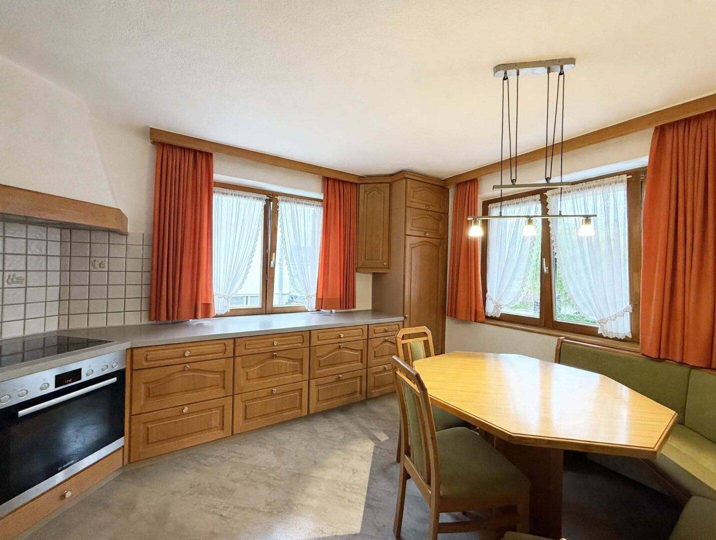 Traditionelle Küche mit Holzschränken, Einbauherd und Essbereich mit Eckbank, strahlt Gemütlichkeit aus.