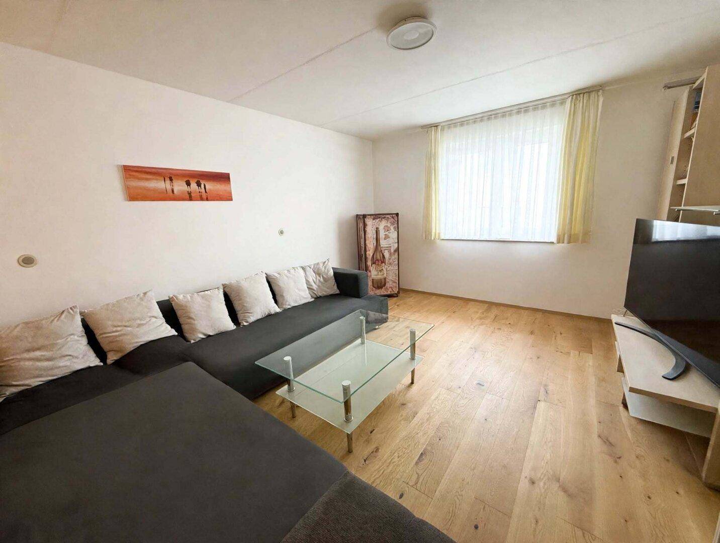 Geräumiges Wohnzimmer mit großem Ecksofa, Glastisch und hellem Holzboden, ideal zum Entspannen.